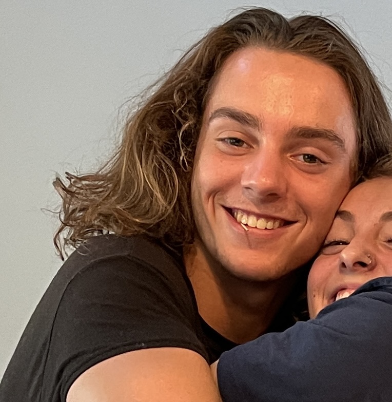 Two people with long hair are smiling and embracing each other closely.